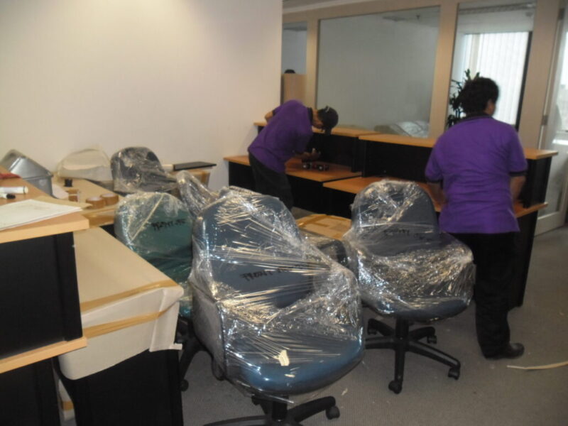 Tim Zetta Movers membungkus kursi dan meja kantor dengan plastik wrapping saat proses pindahan kantor.